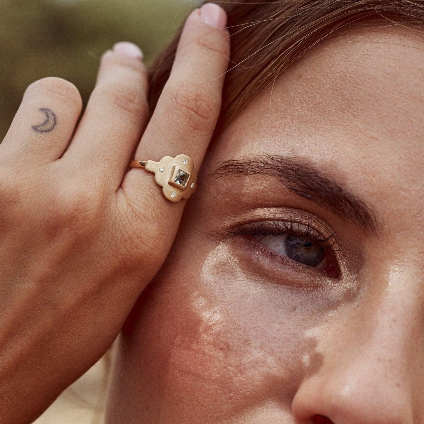Mujer con la mano apoyada en la cara mostrando el Anillo Isolda. Hecho con oro Fairmined de 18k y una preciosa aguamarina natural talla princesa.