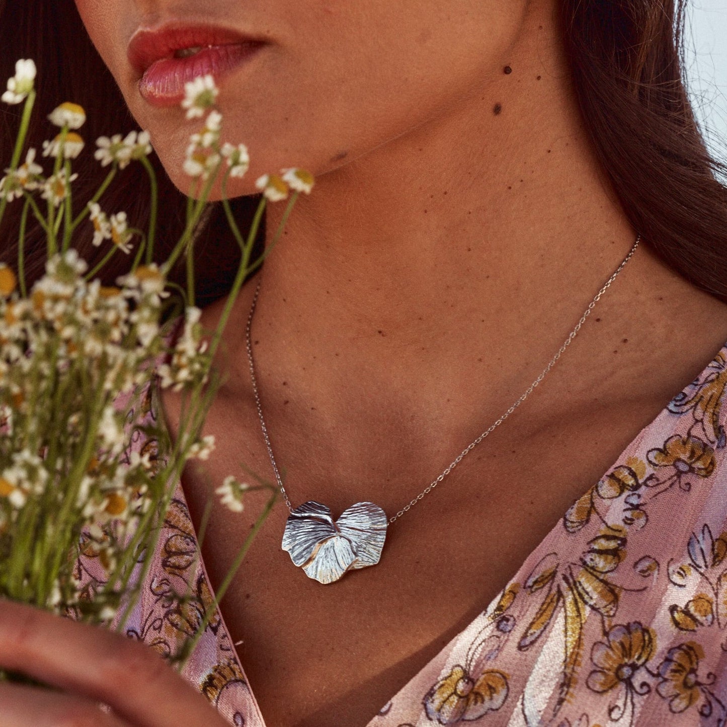 Mujer con un ramo de flores que muestra el collar Orchid, fabricado en plata de ley.