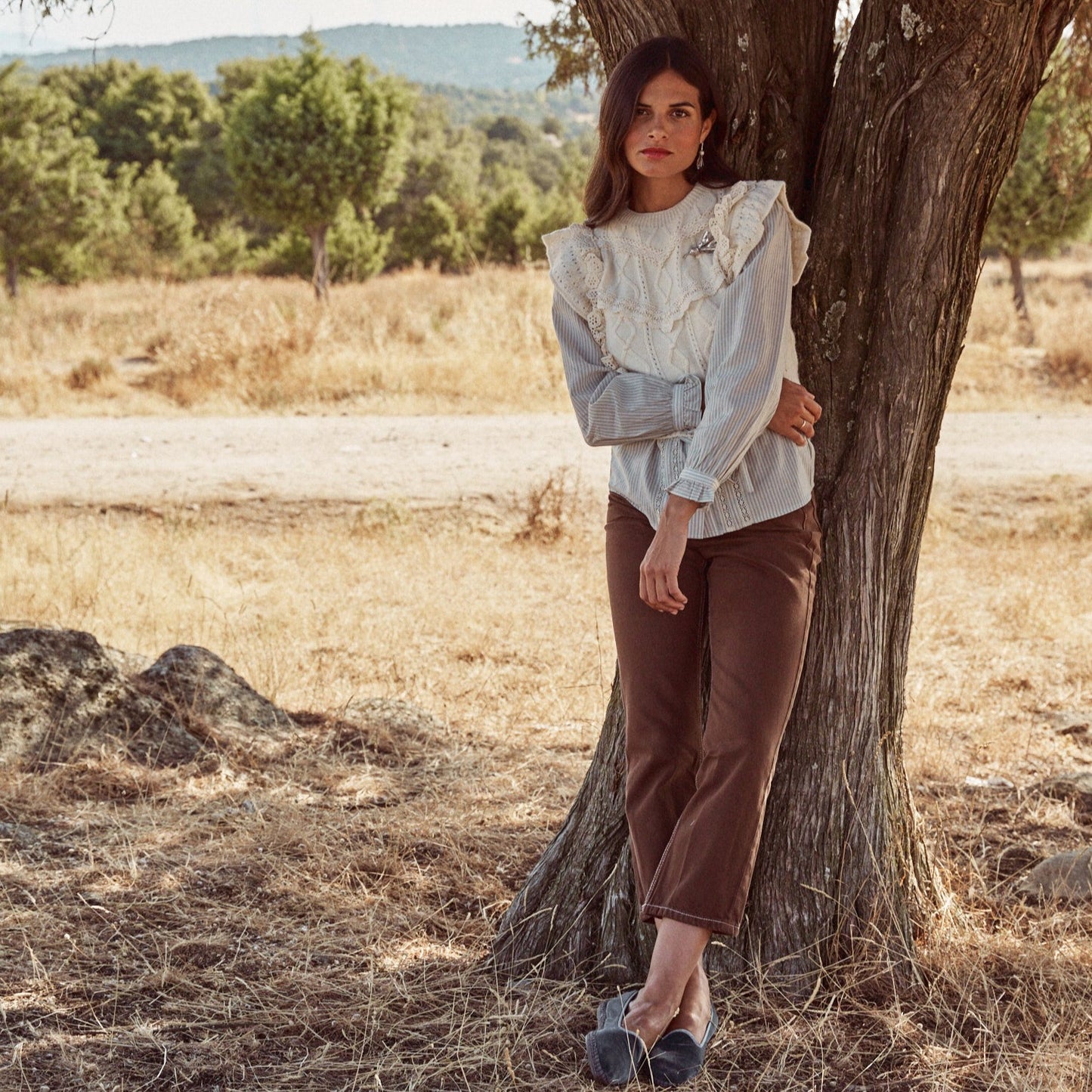 Mujer posando apoyada en un arbol con el broche Autumn Flower y los pendientes a juego. Son joyas hechas a mano con plata de ley con forma de flor otoñal.
