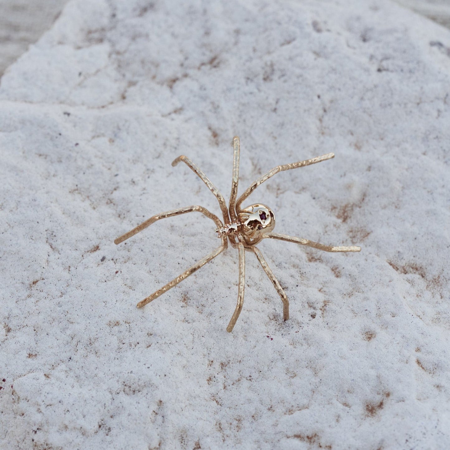 Detalle del Pin Spider, joya con forma de araña, fabricada en oro macizo de 9k con dos rubíes naturales.
