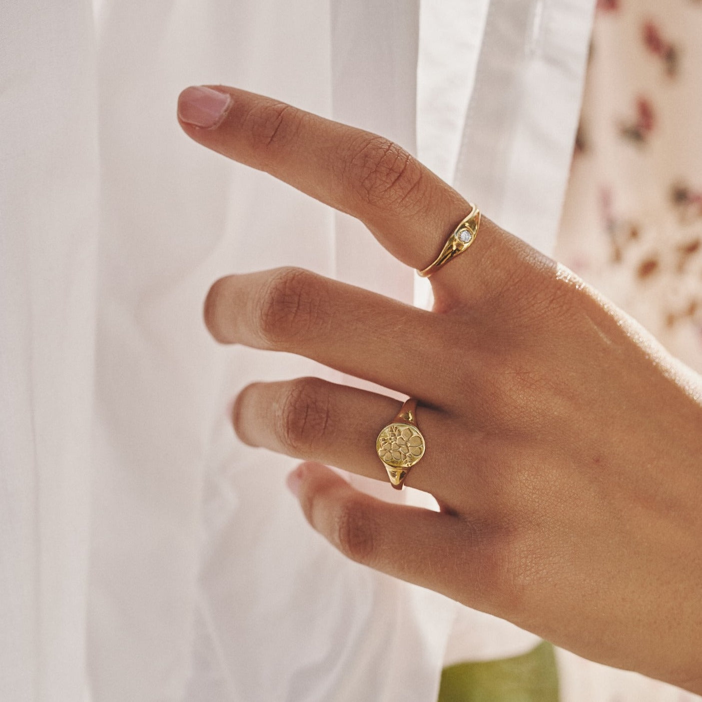Mano de mujer acariciando una tela y mostrando el anillo Loretta junto al sello Allegra, ambos fabricados artesanalmente por LA MUSA.
