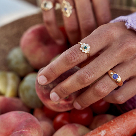 Mujer colocando fruta en una cesta mostrando el anillo Simone. Joya de oro de 18k con un zafiro azul talla redonda.