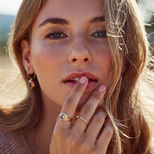 Mujer con la mano sobre los labios mostrando el anillo Ophelia, de oro Fairmined de 18k y con una prasiolita natural.