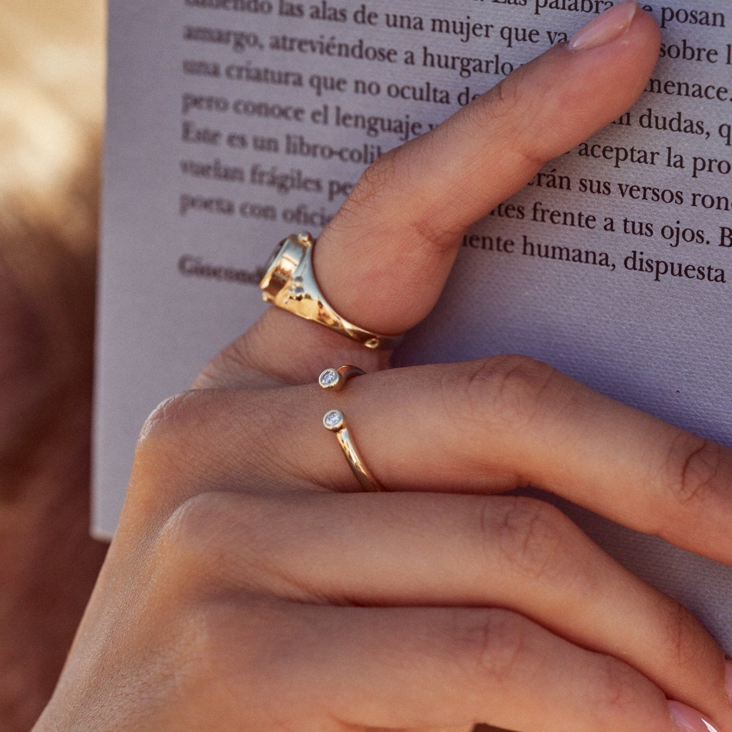Mano de mujer sujetando un libro, donde se observa el Anillo Amelia, con su aro abierto y dos diamantes en los extremos.
