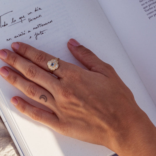 Mujer con la palma de la mano sobre un libro, mostrando el Anillo Isolda. Muestra la pieza fabricada en oro Fairmined de 18k con una aguamarina natural talla princesa y cuatro diamantes.