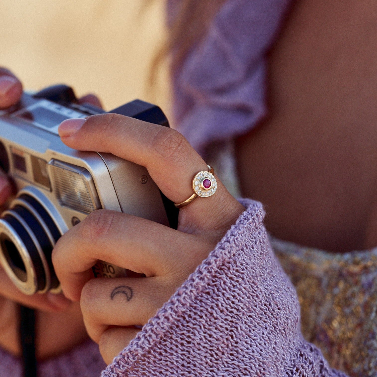 Mujer sujetando una cámara de fotos y mostrando el Anillo Marie, en el que destaca su rubí rodeado de diamantes.