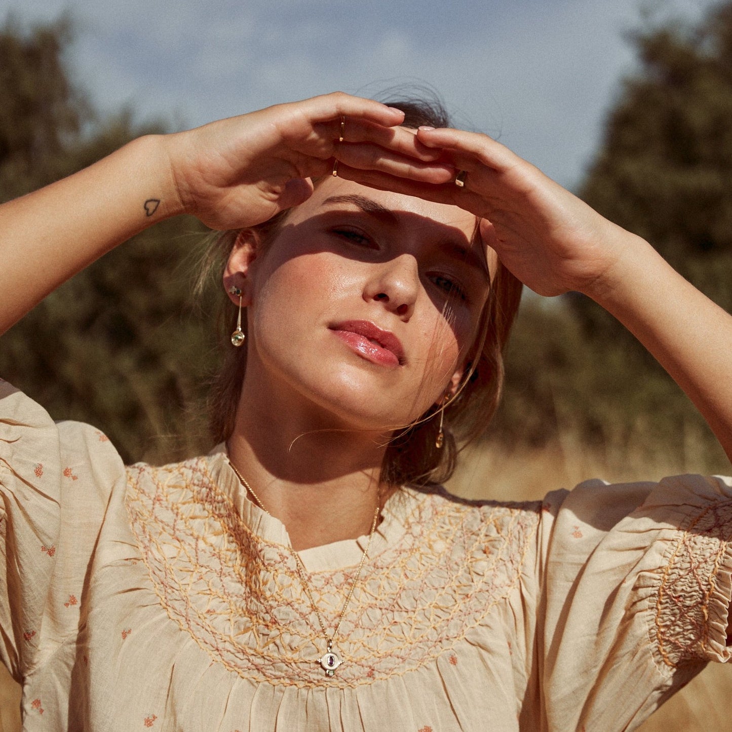 Modelo luciendo los pendientes Juliette en su versión en largo. Destaca el resplandor del oro de 18k  con la luz del sol