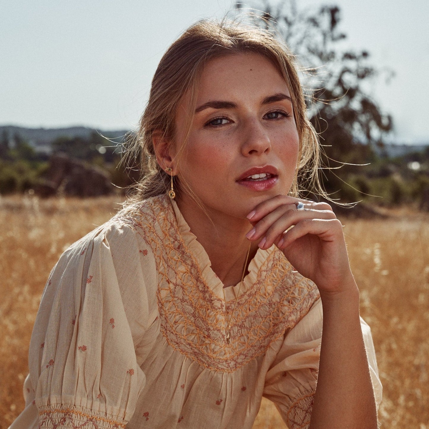 Modelo en un campo de espigas doradas mostrando los pendientes Juliette. Son pendientes desmontables y en la foto aparecen en su versión en largo. De oro macizo de 18k con dos esmeraldas naturales talla redonda cada uno.ç