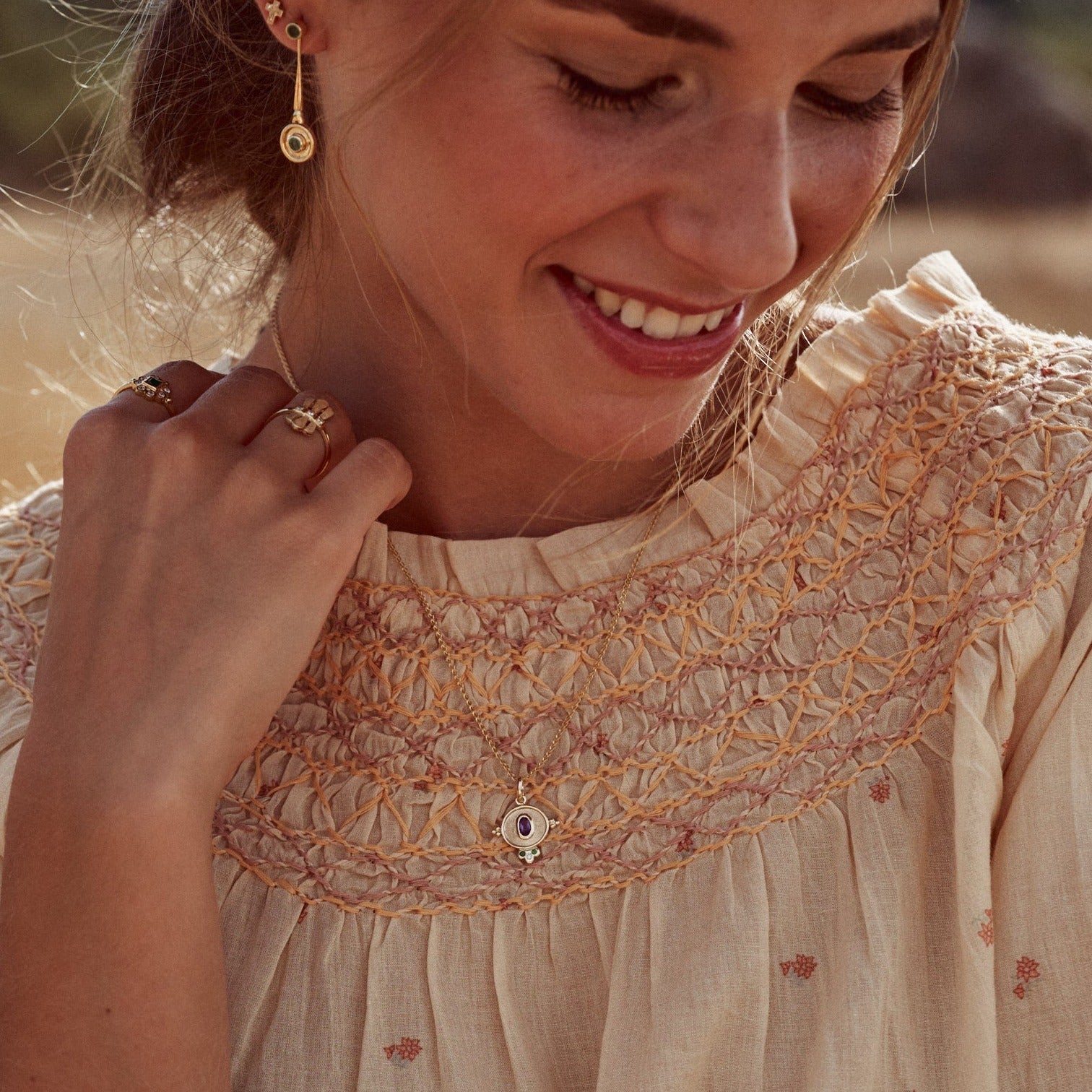 Imagen de la modelo sonriendo y mostrando la Medalla Marianne. Preciosa creación hecha a mano donde destaca el contraste creado por el oro macizo de 9k, su amatista, granates verdes y diamante.