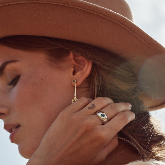 Mujer con sombrero tocándose el pelo y mostrando el anillo Liliana elaborado en plata de ley, con una montura de oro macizo de 9k y un topacio London natural.