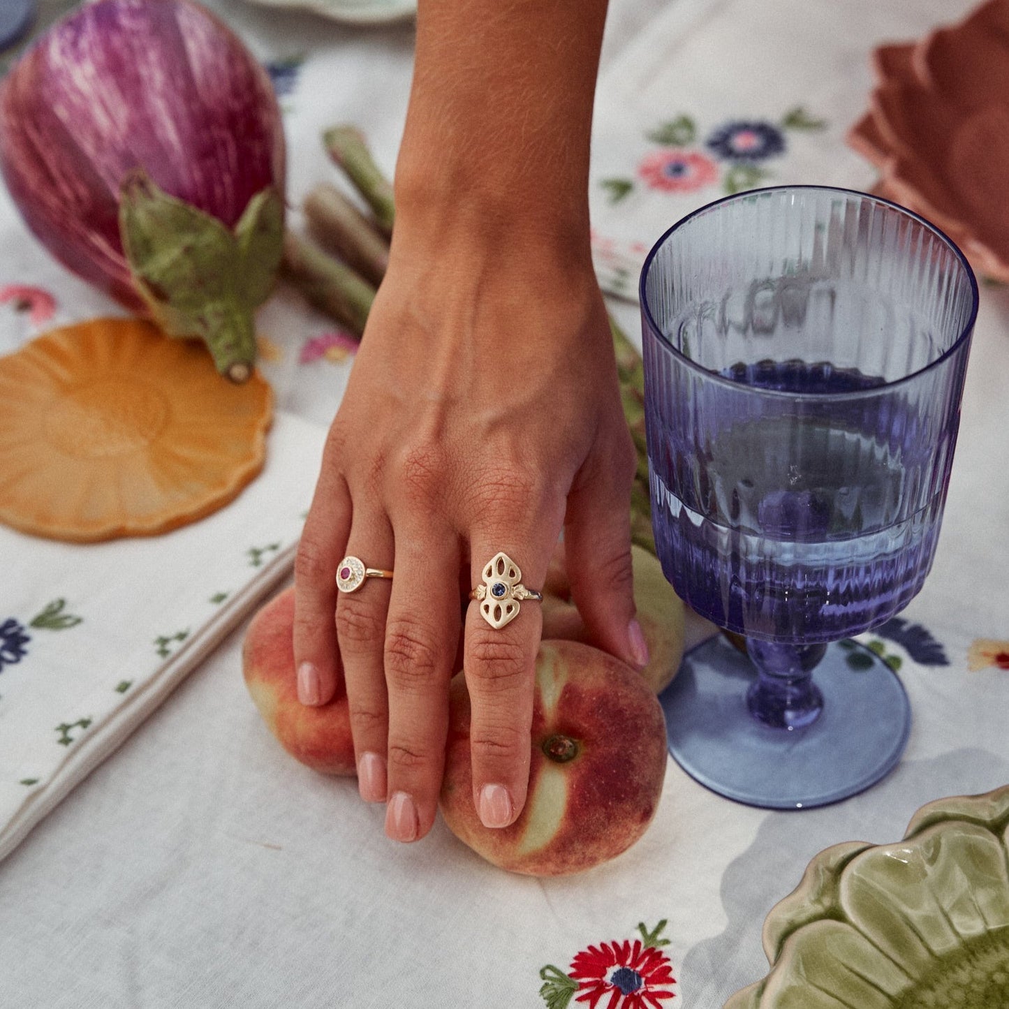 Mujer colocando fruta en una mesa con el anillo Greta . Deja ver el bonito contraste del oro de 18k con el zafiro azul.