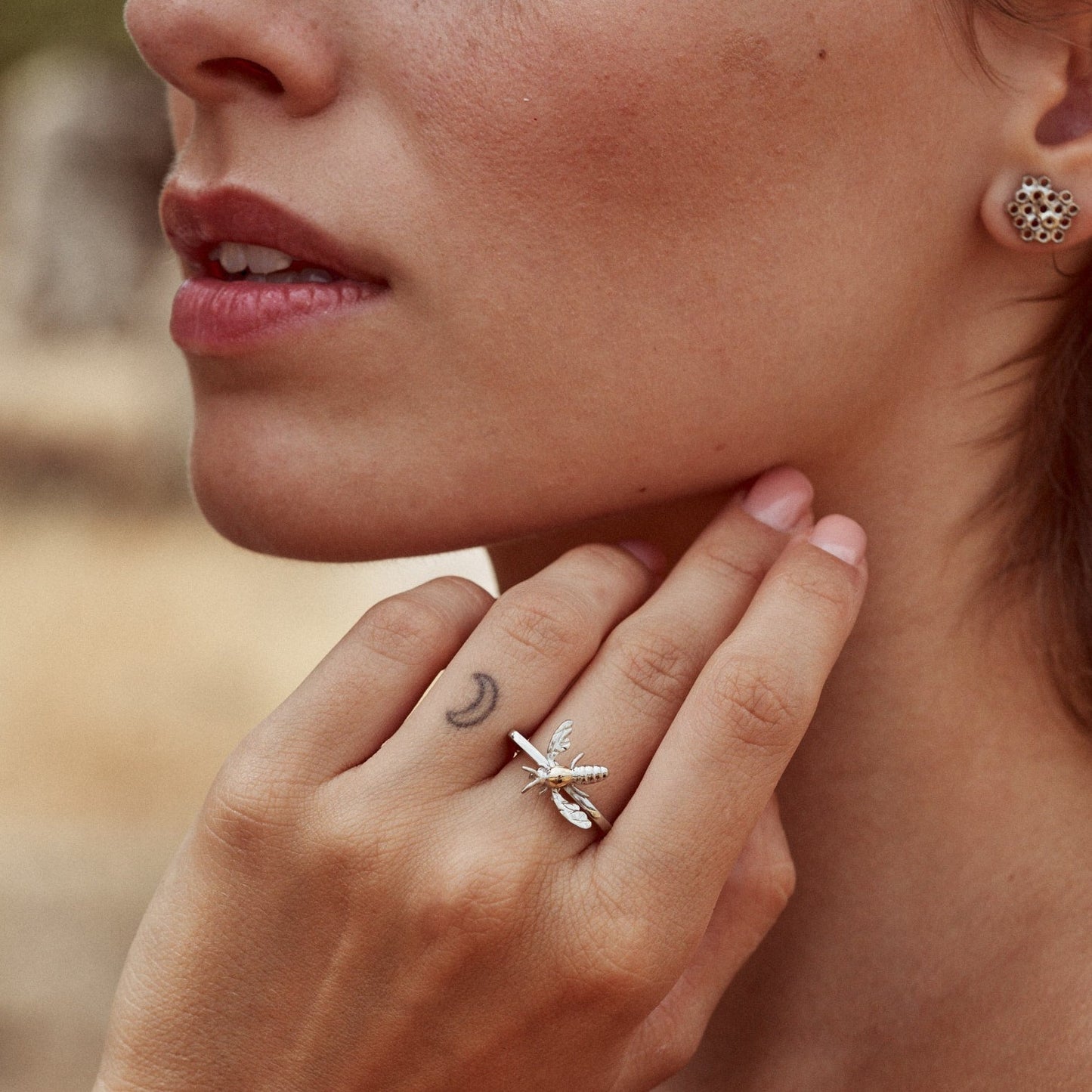 Mujer con la mano apoyada en el cuello, mostrando el anillo Bee, con forma de abejita.