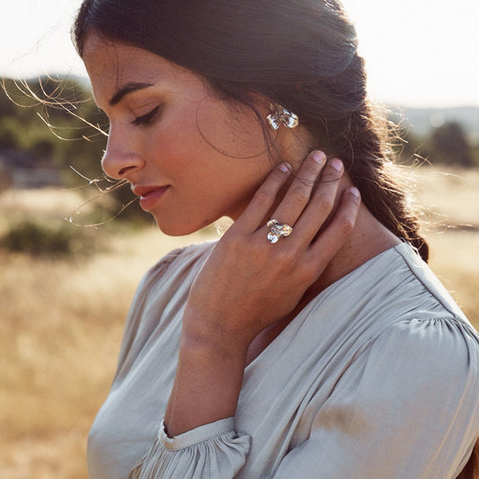 Imagen de una mujer posando en el campo con el anillo de Floralis, joya de plata de ley con forma de flor.