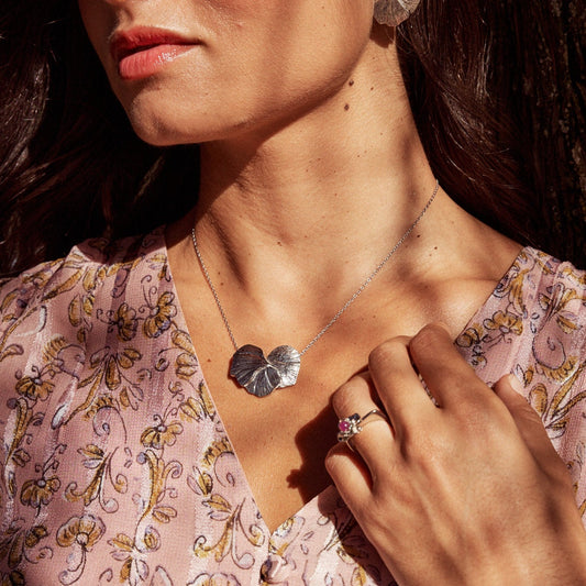 Mujer apoyando su mano en el cuello de la blusa, mostrando el Anillo Isabela. Joya con forma de flor, fabricada en plata de ley con una bolita de rubí natural.