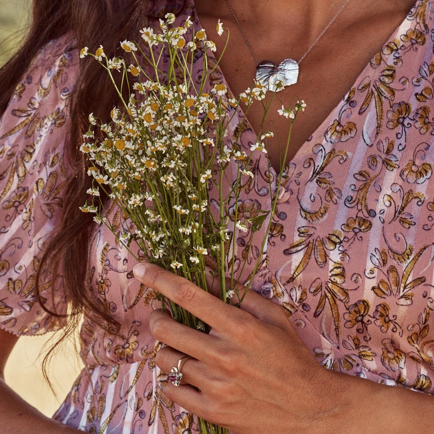Mujer sujetando un ramo de flores y mostrando el Anillo Isabela, anillo con forma de flor y aro recto, que lleva una pequeña bolita de rubí natural. Elaborado en plata de ley.