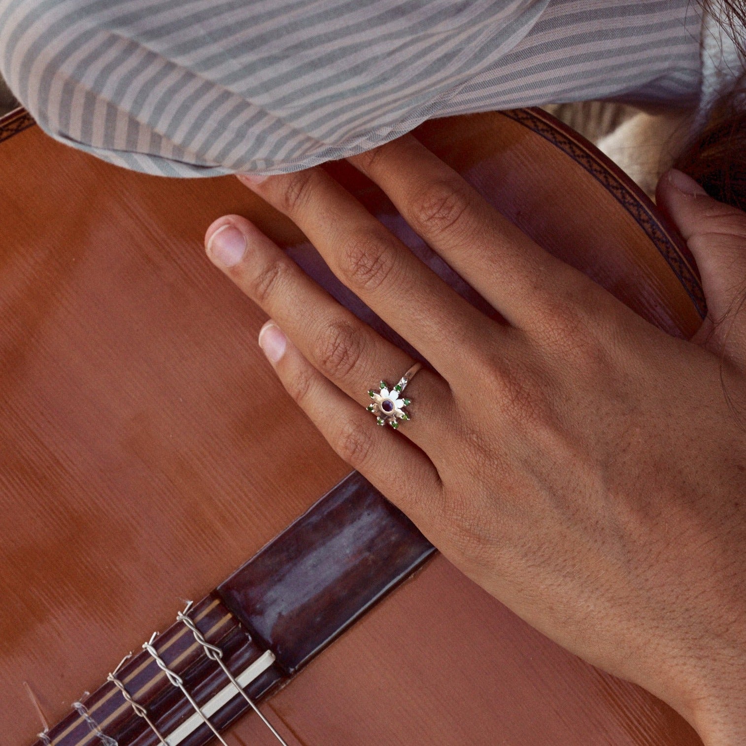 Mujer sujetando una guitarra y mostrando el anillo Yvette, con forma de flor estrellada. Fabricado con plata de ley, granates verdes y una amatista.