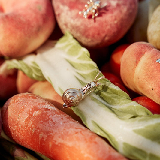 Pin Caracol sobre un cesto de fruta y verdura. Es un pin de oro de 9k.